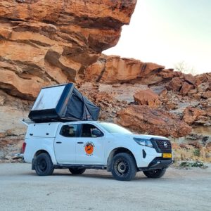 Nissan Navara 4x4 with hardtop tent at on campsite infornt of boulders