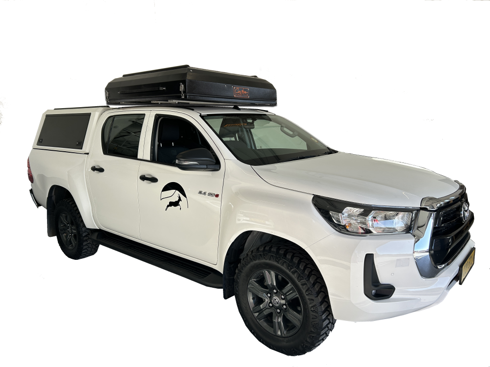 Weißer Toyota Hilux Allrad Mietwagen mit einem Hardtop Dachzelt drauf.