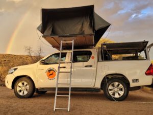 4x4 pickup truck with rooftop tent under rainbow
