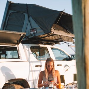 Woman preparing meal infront of 4x4 rental car with hardtop rooftop tent on.