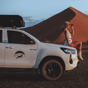 Woman on bonnet of rental car infront of dune in Namibia