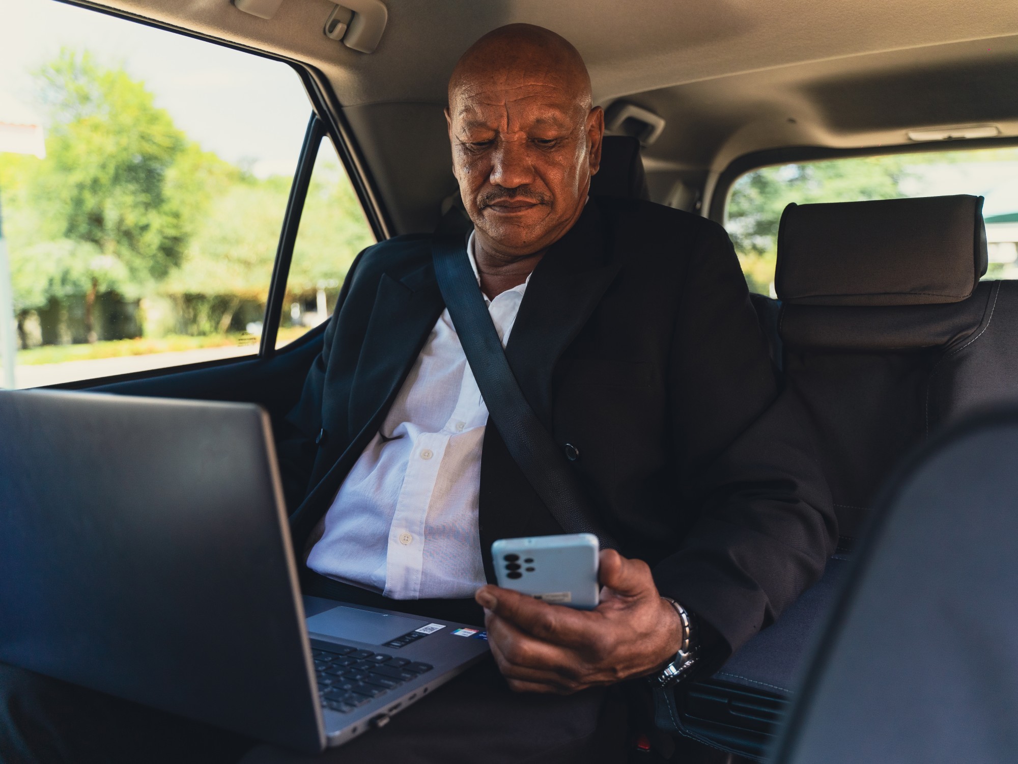 Business man in back of car with laptop and phone
